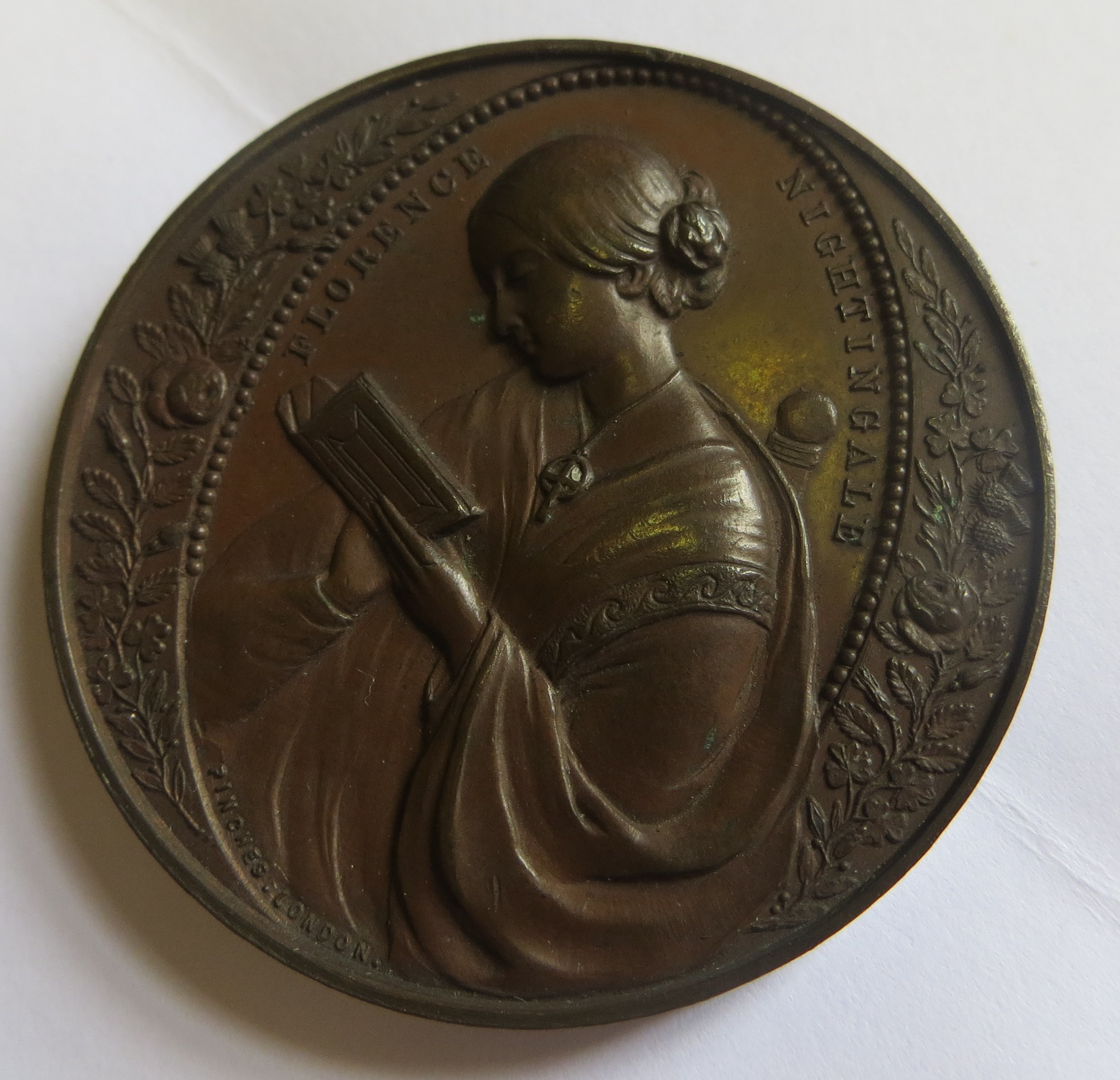 Circular medal showing an embossed image of Florence reading a book.