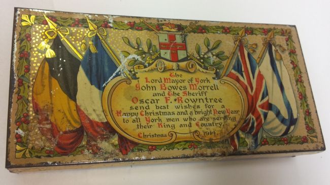 Tin decorated with flags and the inscription: ‘The Lord Mayor of York, John Bowes Morrell and the Sheriff, Oscar F. Rowntree, send best wishes for a Happy Christmas and a bright New Year to all York men who are serving their King and Country. Christmas 1914'.