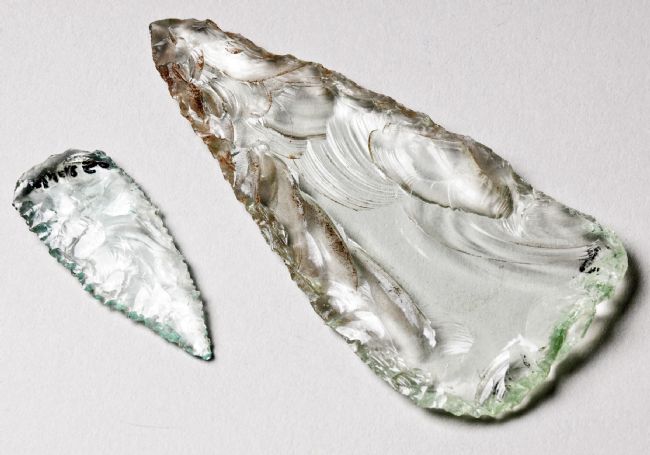 Two glass spearheads, one much bigger than the other.  Both are wider at one end and have been knapped to a point at the other.