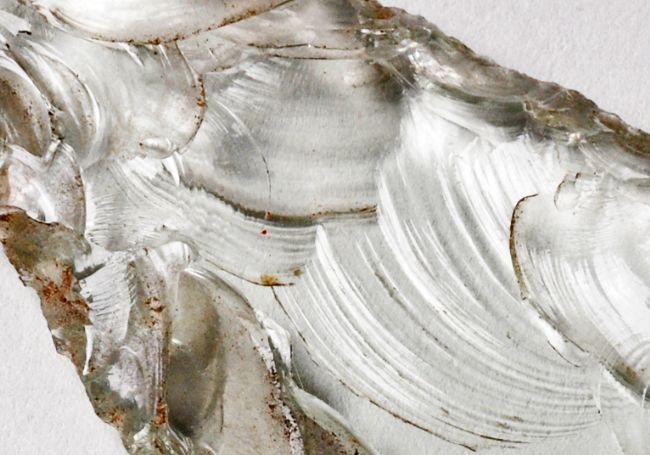 Close up shows the flake scars of parallel curved lines where flakes of glass have been removed.