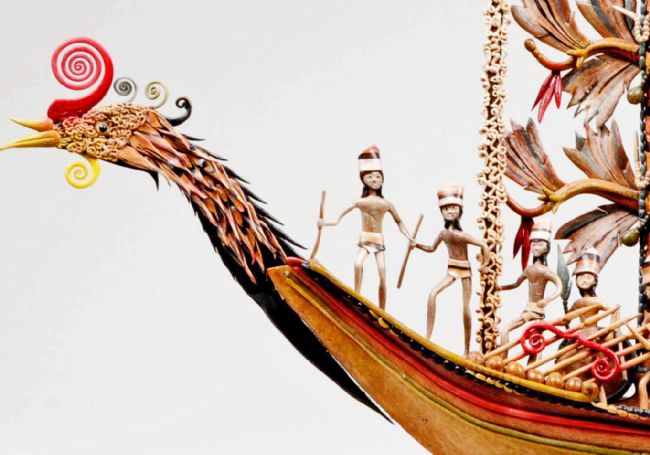 The prow of the boat is in the shape of a bird head and several figures wearing loin cloths and head dresses can be seen.