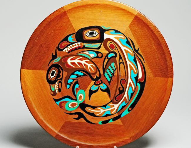 Killer Whale Souvenir Plate of Cedar Wood.  The wood ranges from golden to tan coloured.  A First Nations styalised  Whale and baby whale are painted in the centre